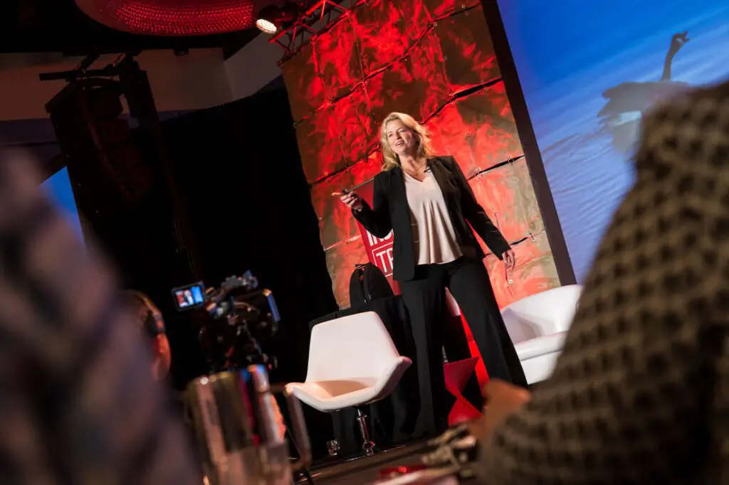 Speaker presenting on stage with red backdrop.