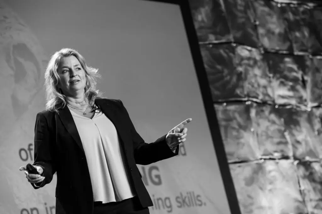 Woman speaking on stage with presentation screen.