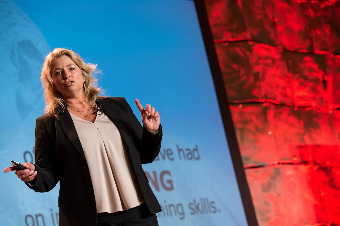 Speaker presenting on stage with red backdrop.
