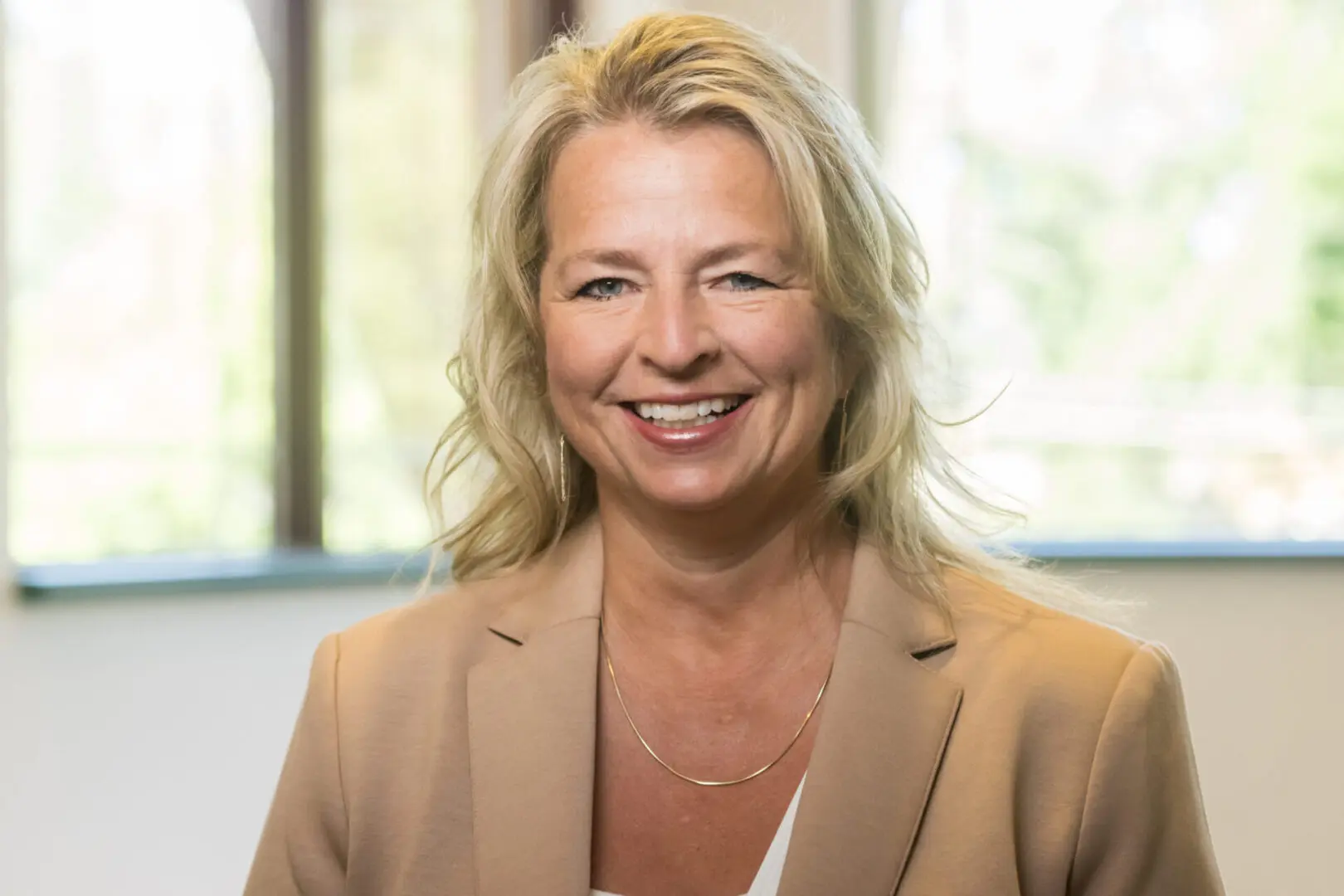 Smiling woman in beige blazer indoors.