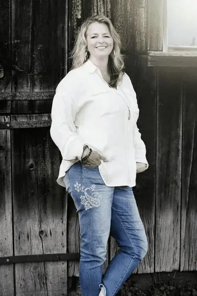 Woman in white shirt, jeans, against wooden wall.
