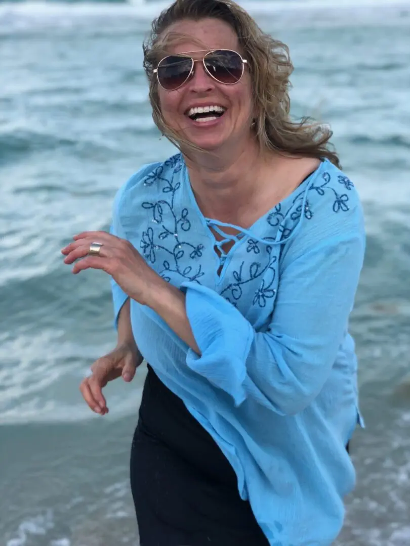 Smiling woman in blue by the ocean.