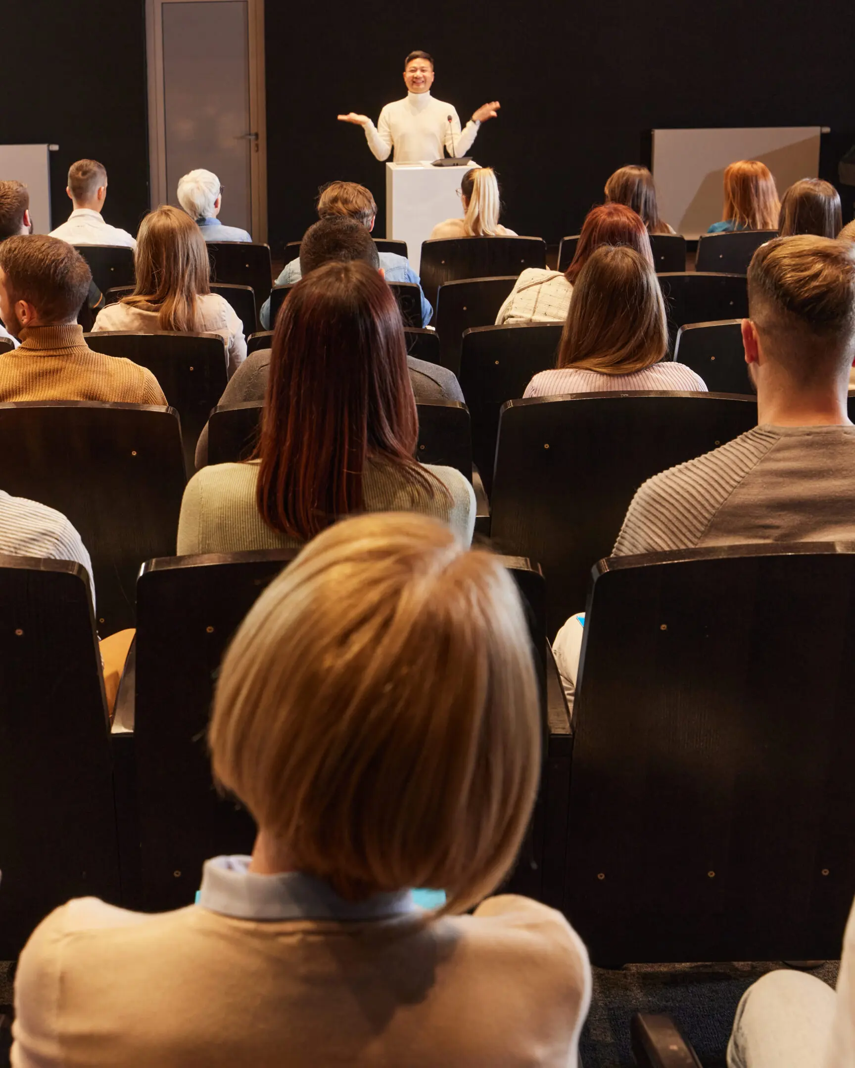 Rear view of large group of people listening to a speaker on press conference in convention center.