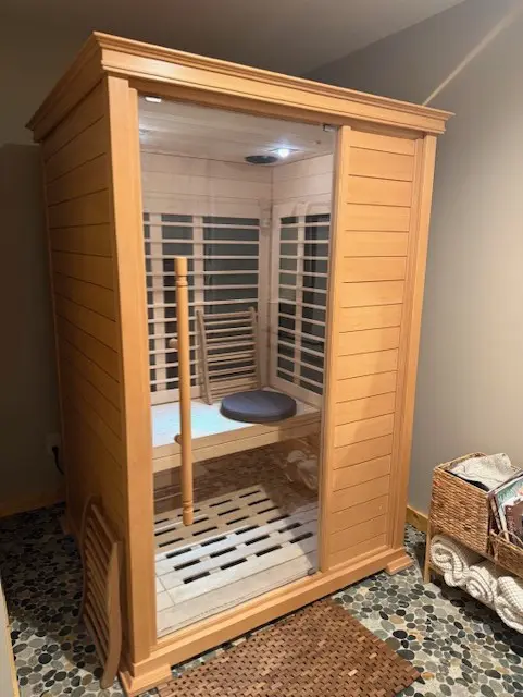 A wooden infrared sauna cabin with glass door in a cozy room.