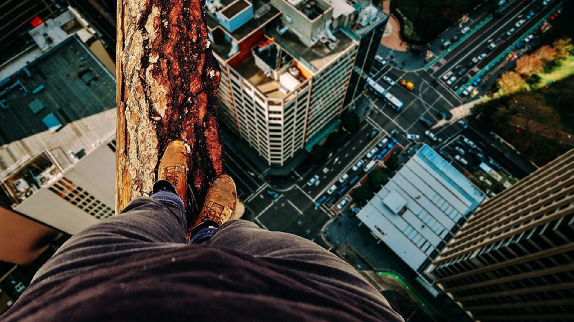 Person standing on edge of tall building looking down at city street below.