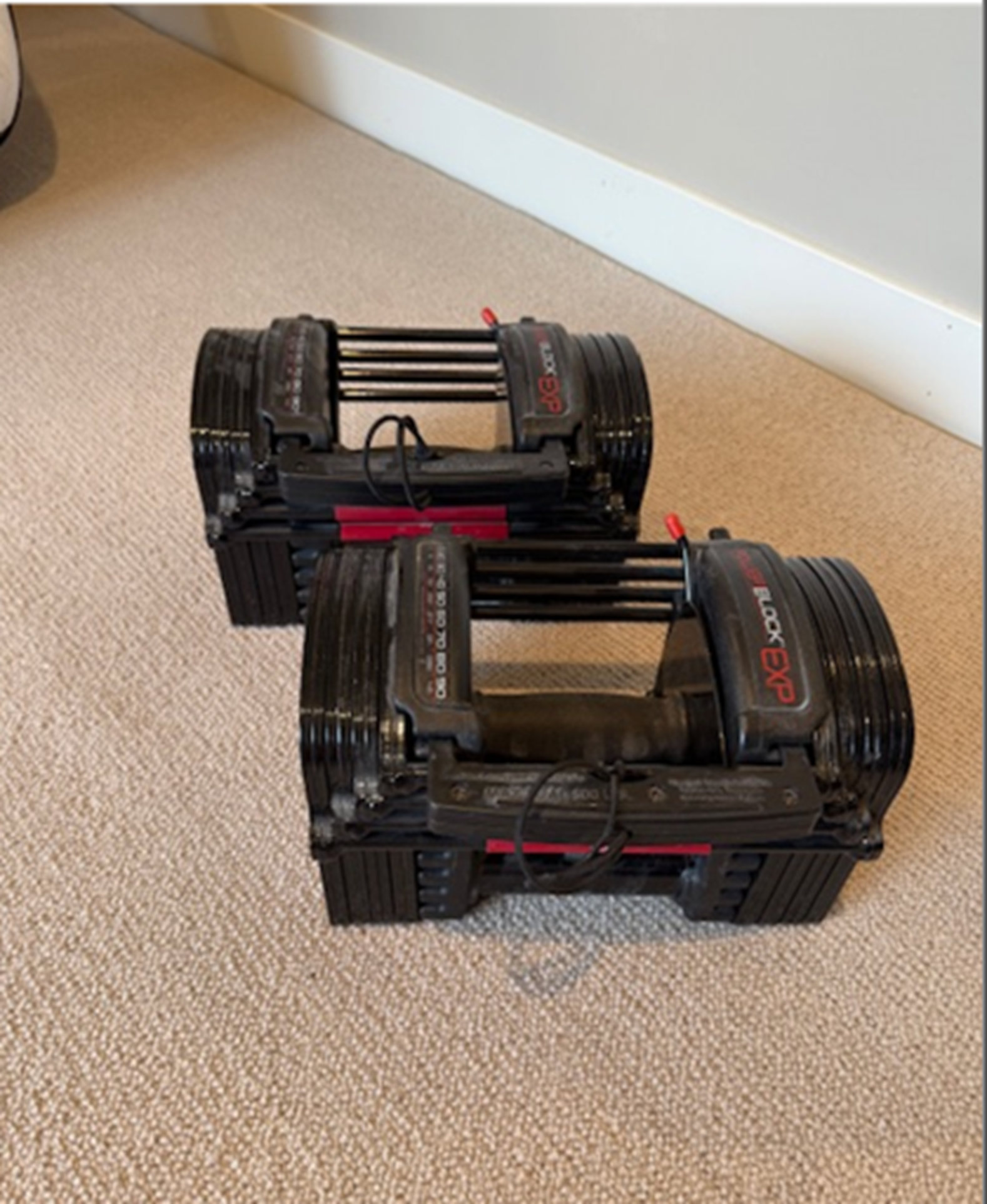 Adjustable dumbbells placed on a carpeted floor near a wall.