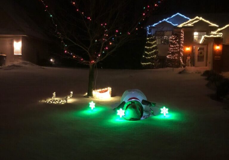 Snowman and lights in snowy yard at night.