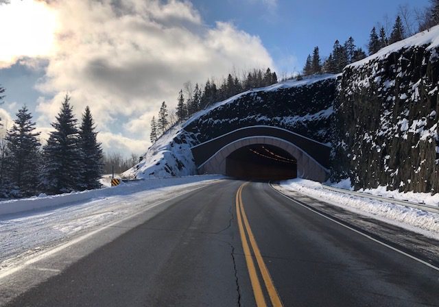 Snowy road leading into mountain tunnel.